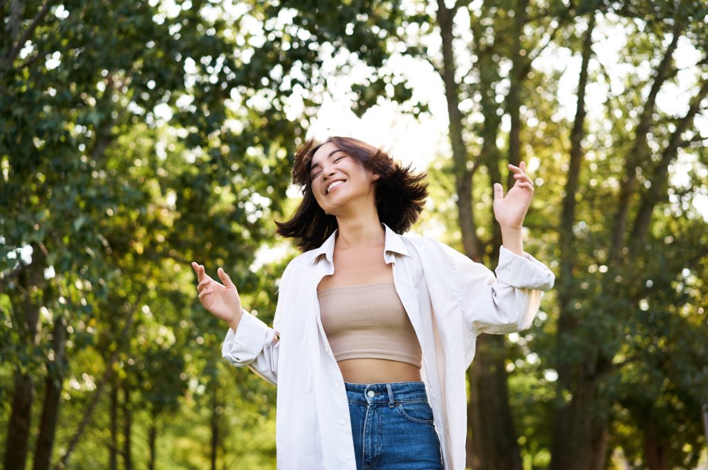 Happy people. Carefree asian girl dancing and enjoying the walk in park, feeling happiness and joy, triumphing.