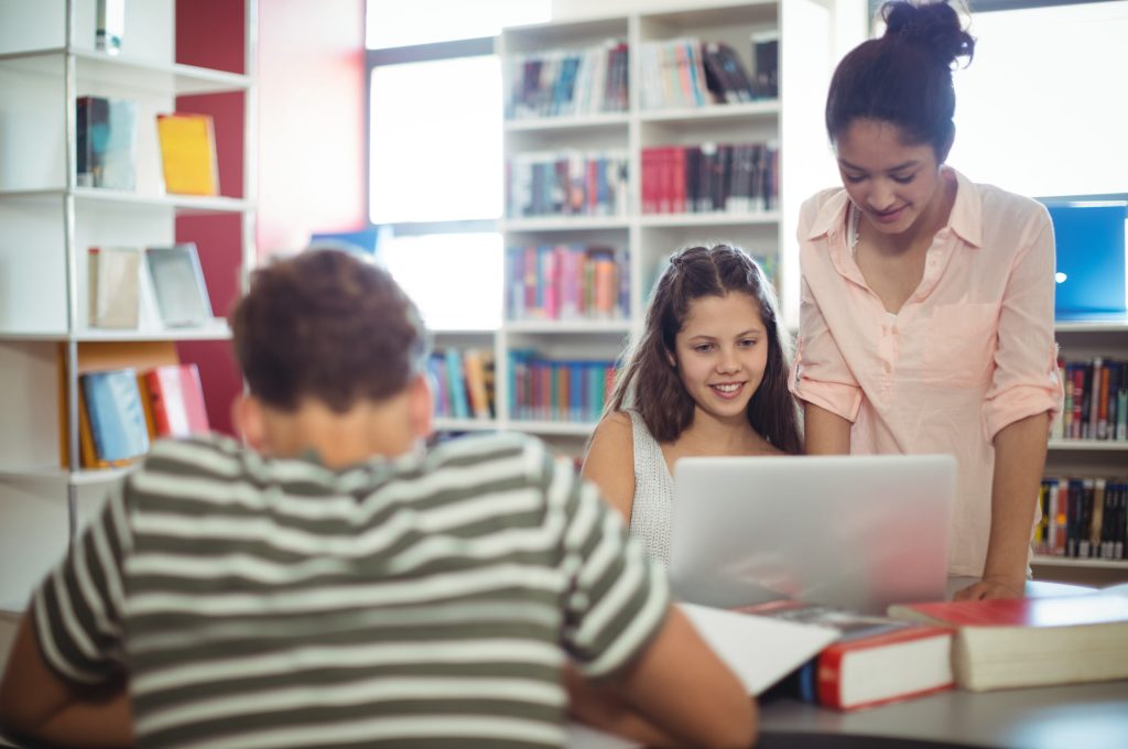 Happy students using laptop in library at school