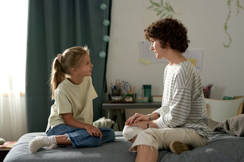 Mother having openly conversation with her daughter while they sitting on bed in bedroom